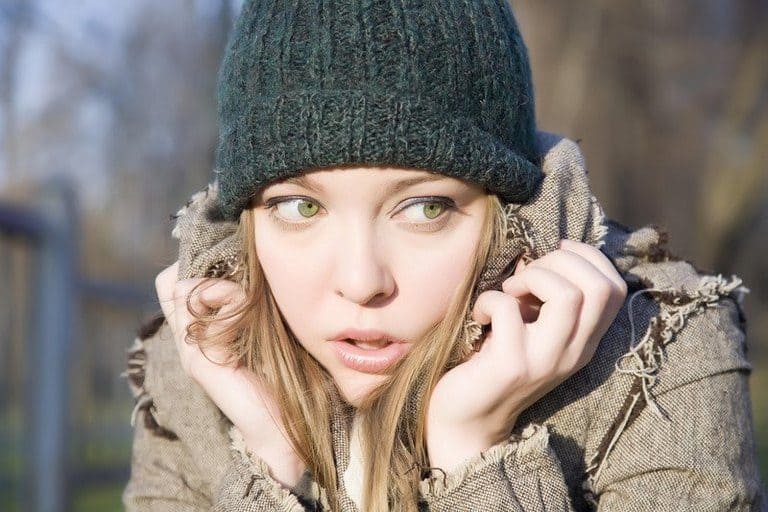 Woman in a beanie slouching with her hands around her face as if she is trying to shut out the world.