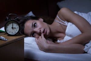 Woman lying in bed awake at night watching the clock.