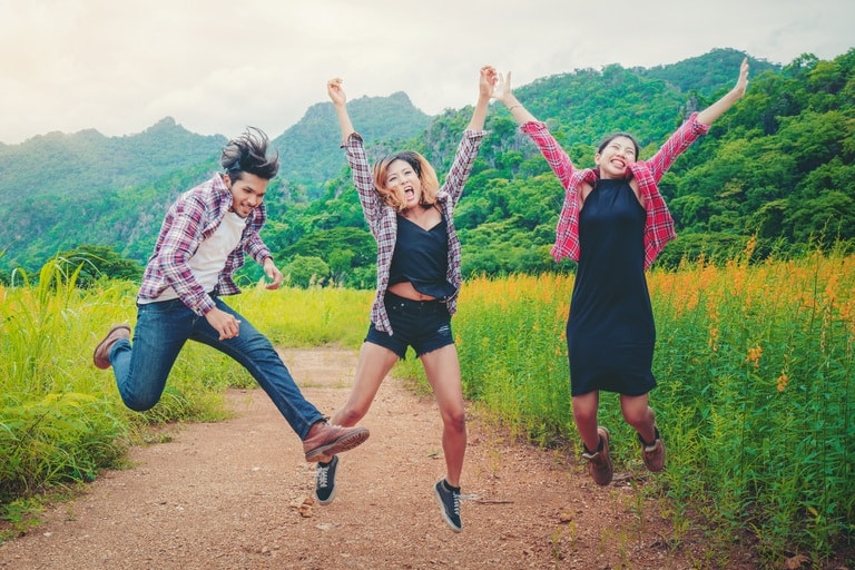 Group of happy young people jumping in the air while traveling in mountain and nature trail.