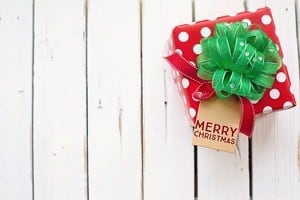 Red gift with green bow on a white wood background