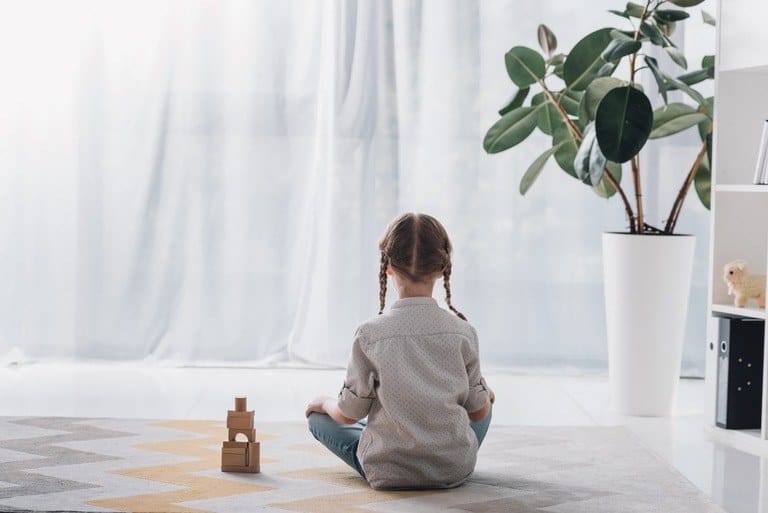 Little girl sitting alone on the floor with her back to the camera.