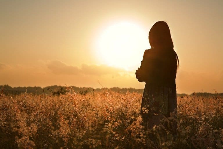 Woman standing in field of flowers, arms folded at sunset