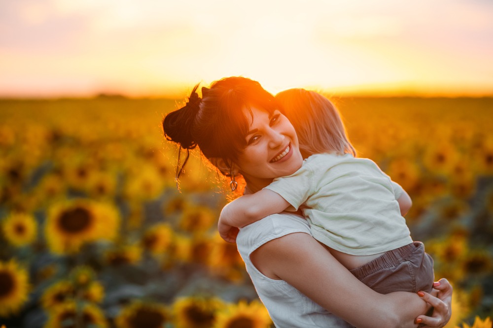 Mom and son holding toddler son in sunflower field at sunset