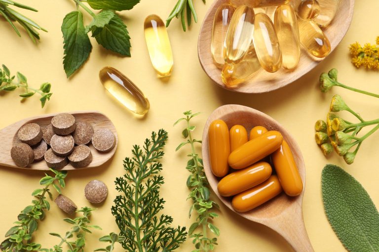 Different pills and herbs on pale orange background, flat lay.