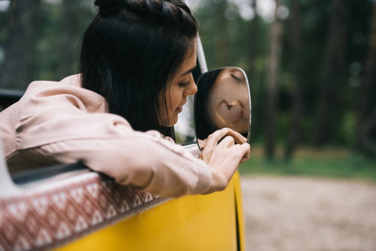 girl leaning out of the passenger window of a VW microbus, drawing a heart in the rear view window.