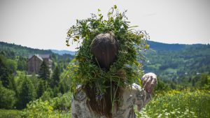 A woman wearing a crown of wildflowers and weeds looks out over the land below, an image of the spiritual meaning of wildflowers.