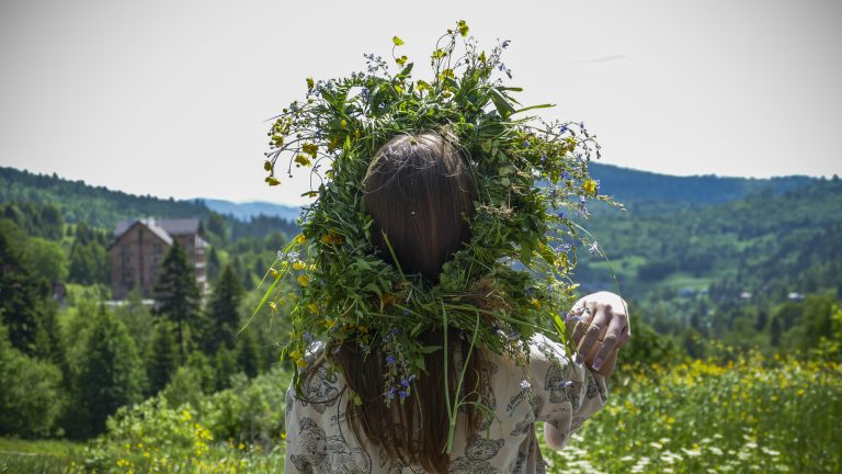 A woman wearing a crown of wildflowers and weeds looks out over the land below, an image of the spiritual meaning of wildflowers.