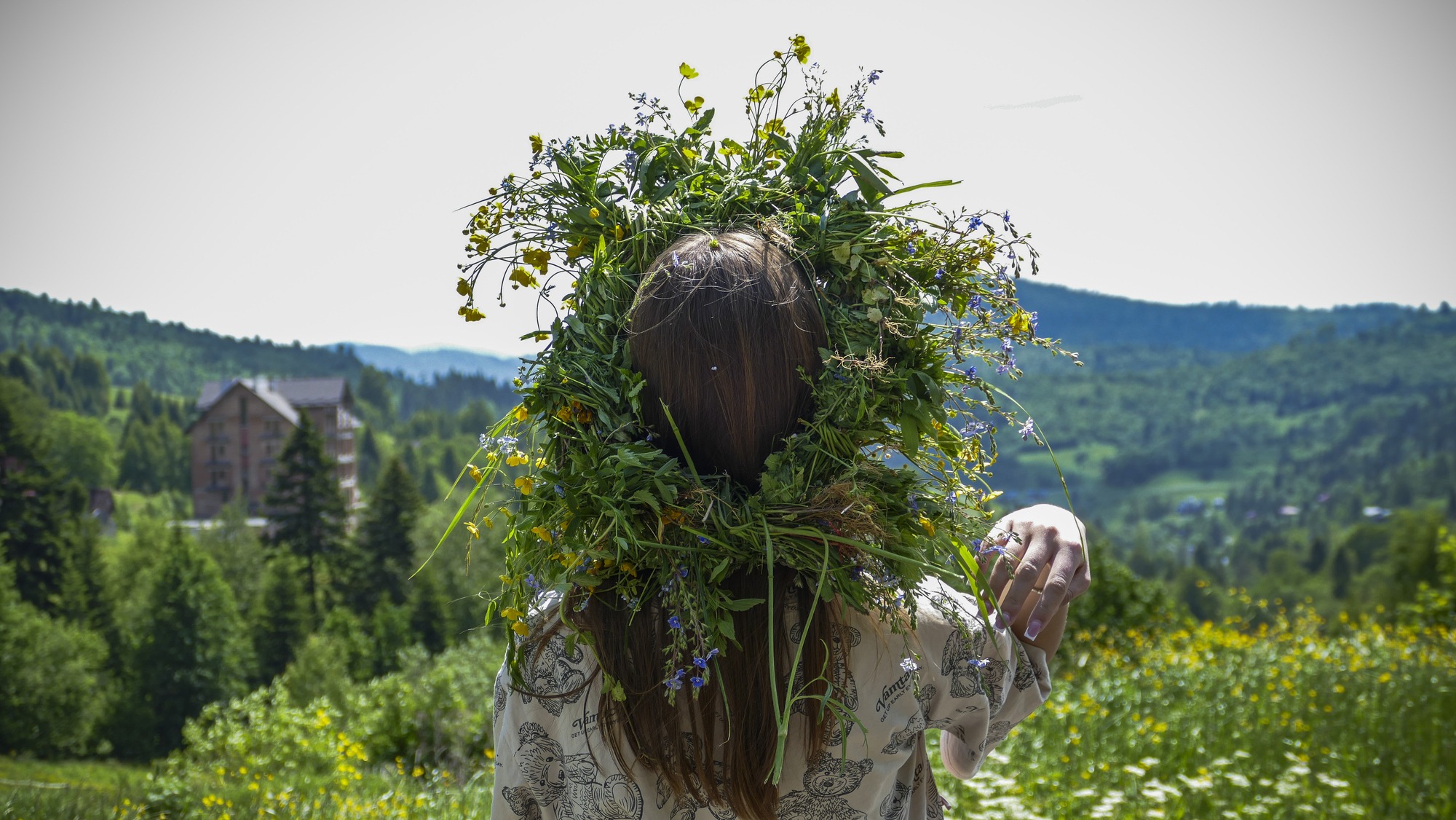 A woman wearing a crown of wildflowers and weeds looks out over the land below, an image of the spiritual meaning of wildflowers.